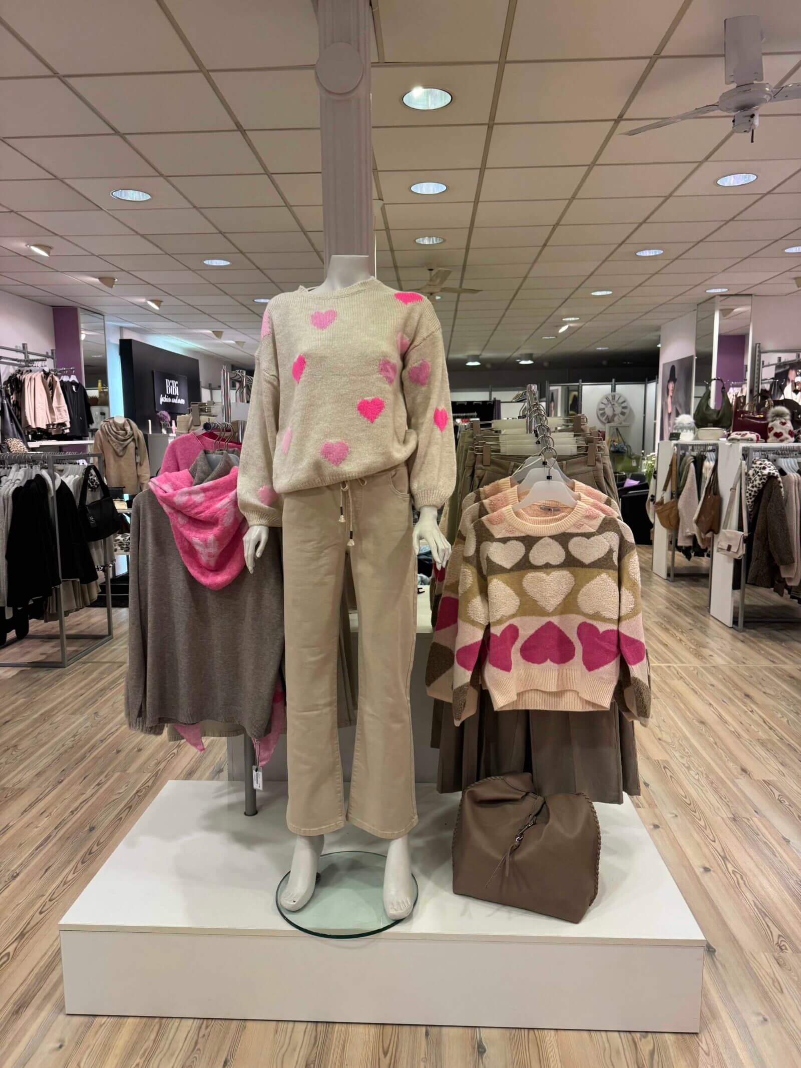Eine Schaufensterpuppe trägt beige Kleidung und einen Pullover mit rosa Herzen im Geschäft